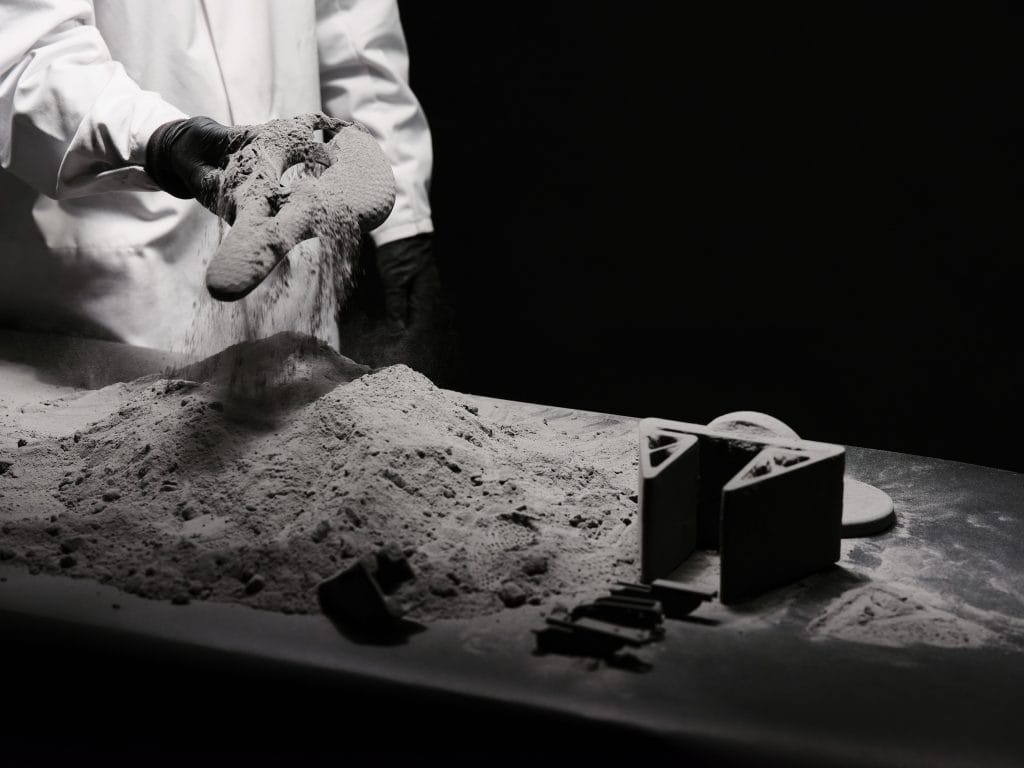 Man holfing a tpu material bike seat next to a table of thermoplastic polyurethane powder and other tpu material 3d printed parts